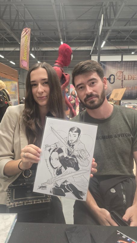 Deux personnes tiennent un dessin d'un super-héros en noir et blanc dans un salon.