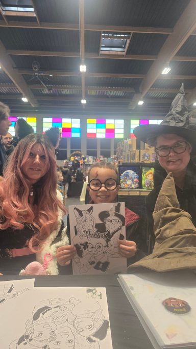 Trois personnes posent avec des dessins lors d'un événement animé.