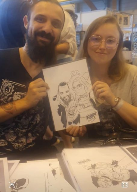 Un homme et une femme tenant un dessin humoristique à un événement.